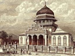 Ilustrasi berwarna dari sebuah masjid dengan kubah besar di atasnya. Masjid ini memiliki arsitektur tradisional dengan detail rumit, termasuk serangkaian lengkungan di pintu masuk yang didukung oleh tiang-tiang. Di sekeliling masjid terdapat pagar rendah. Di latar depan, terlihat beberapa orang dan anak-anak yang sedang berkumpul, menunjukkan suasana yang ramai. Langit di atas masjid dipenuhi awan, menambah kesan dramatis pada gambar.